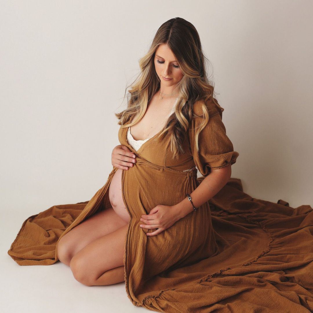 a pregnant woman sitting in long flowing clothes for maternity photos