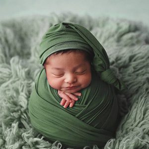 Professional photo of a newborn wrapped in a green cloth with a slight smile