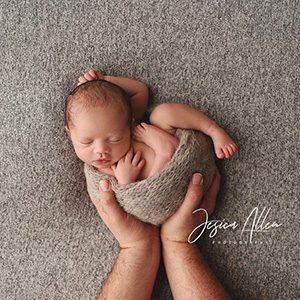 A newborn photo shoot with a parent holding their baby while he lays down