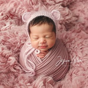 A photoshoot with a newborn in pink cloth wrapping and a fluffy pink blanket