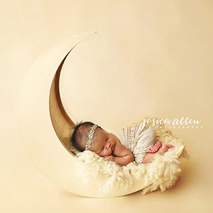 A photoshoot with a newborn laying on a crescent moon shaped rocker and yellow blanket